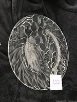 Oval clear glass serving plate with embossed winter berry and leaf pattern on a black fabric background, no chip or damage visible.
