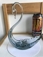 Front angle view of the vintage light blue glass swan figurine placed on a white circular surface with a Monster energy drink can beside it for size reference.