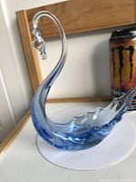 First light blue glass swan shown on a white and wooden surface with a Monster energy drink can in the background for scale.