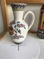 Right side of small ceramic jug showing colorful hand painted floral designs and neck and rim decoration