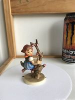 Left and front angle view of girl on apple tree branch figurine next to a can for size comparison.