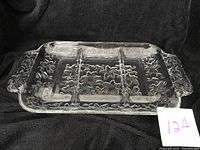 Clear rectangular glass server plate with three divided sections and decorative leaf pattern throughout, including the handles. Photographed against a dark backdrop to highlight etching details.