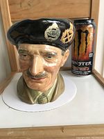 Front view showing detailed face and beret with insignia, can of Monster energy drink placed for scale.