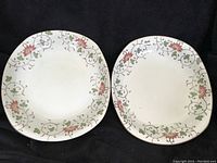 Pair of square plates with floral vine borders on a dark background