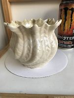 Front view of cream porcelain vase showing wavy rim and textured body near a beverage can for size comparison.