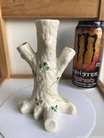 Front view of the cream Belleek porcelain tree stump vase with shamrocks, next to a Monster energy can for scale.