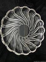 Top-down view of a clear crystal platter showing the swirl design and scalloped edge.