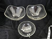 Three clear glass bowls including two square bowls and one round bowl with three glass stub feet. Photographed to show the set contents and overall condition.