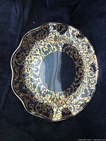 Photo showing the front of the vintage glass plate with black background highlighting gold decorative trim and scalloped edge.