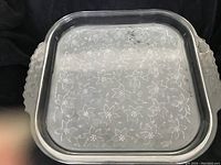 Top view of a large square transparent glass platter with etched flower and leaf pattern and leaf motif handles.