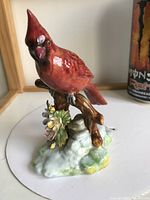 Front view of a glossy red cardinal porcelain figurine perched on a brown branch with flowers and greenery on the base.