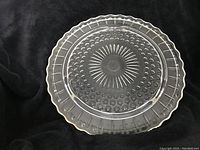 Top-down view of the clear glass serving plate showing the textured dot and sunburst pattern and scalloped edge.