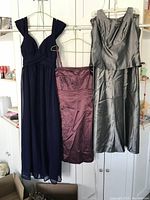 Three formal dresses hanging on a rack: navy blue long dress, purple knee-length dress, gray sleeveless dress