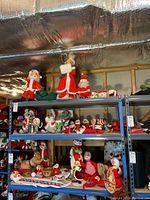 Wide view of shelving with multiple Annalee dolls, Santa figurines, and mugs arranged in holiday display.