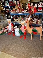 Four large Annalee Christmas figures on floor in front of shelving, including Mrs. Claus, Santa, snowman, and reindeer.