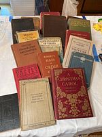 Collection of various antique and vintage hardcover books arranged on a table showing a variety of colors, titles, and conditions.