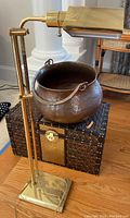 Side view showing the brass floor lamp with adjustable arm and shade, the hammered metal pot placed on top of the decorative lidded trunk.