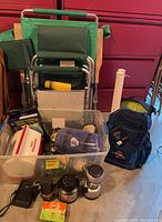 Full view of lot showing green folding chairs stacked, plastic clear bins containing gear, Penn blue backpack, black binoculars and other camping accessories.