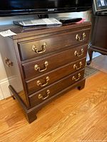 Front view of the wood chest of drawers showing four drawers with brass drop handles and scratches on the surface.