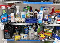 Two shelves filled with assorted cleaning supplies including spray bottles, liquid and powder cleaners, and wipes