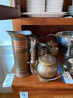 Photo showing three copper items: a tall pitcher, a smaller pitcher, and a rounded tea kettle on a tray with patina and dents.