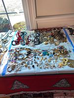 Full view of assorted costume jewelry including earrings, rings, necklaces, bracelets spread on a white cloth on a table by a window.