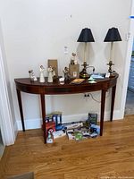 Full view of demi lune table against wall with decorative items on top and various boxed items stored underneath.
