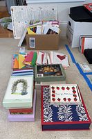 Photo showing a variety of note cards and greeting cards in a box with multiple stacks of boxed cards arranged in rows