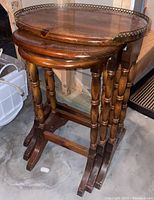 Set of three wooden nesting tables stacked together, showing the rounded tops and turned legs, placed on a concrete floor.