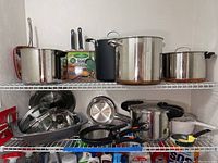Two wire shelves with multiple cooking pots and pans, various sizes and materials including stainless steel and non-stick. Includes lids and cookware accessories visible.