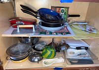 Overall shelf with multiple cookware items including fry pans stacked, strainers, a bacon press, spoon rests and cutting boards to show variety and condition