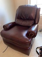 Front side view showing padded chair back, armrests with brass nailhead trim, and leather seat cushion.