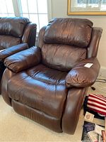 Dark brown faux leather recliner shown from a side angle, highlighting cushioned seat, backrest, and armrest on the left side with visible wear on top of armrest and headrest.