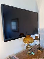 Front view of Sharp 52 inch flat screen TV mounted on wall above wooden surface with vintage lamp and small antique candle holder. Remote controls placed below TV.