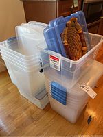 Multiple clear plastic storage bins stacked, some with lids, and a woven wicker basket inside one bin.