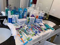 Full overview of oral care items on a bathroom counter including toothbrushes, toothpaste, floss, mouthwash, and cups. Items are new and packaged.