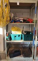 Full shelving unit with wire mesh baskets, green plastic bins with tools, cords, and gloves on shelves