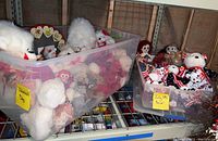 Photo showing two plastic storage totes labeled with hand-written sticky notes 'Valentine's Day' and 'July 4th Decor' filled with various stuffed animals and dolls on metal shelving.
