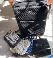 Photo of large black Vera Bradley quilted rolling suitcase with smaller bags clustered at base