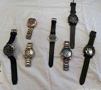 Full view of seven watches, various styles and bands, laid on white cloth