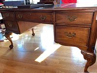 Full view of Sligh wood desk showing brass handles on drawers and carved wood legs.