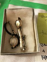 Box containing two ladies watches including a gold Tudor watch and a Gruen watch with a fabric band.
