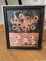 Full front view of the framed mixed media art showing the circular patterns with black raised elements and textured background in black and terracotta.