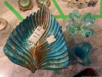 Top view of three art glass bowls including a large leaf-shaped bowl and two smaller decorative bowls on a marble floor.