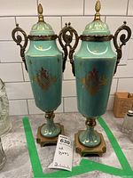 Pair of turquoise porcelain lidded urns with ornate bronze mounts placed side by side on countertop.
