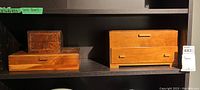 Two light to medium wood tone rectangular wooden storage boxes placed on a shelf, each with drawers and simple handles.