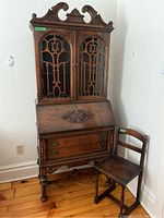 Front view of the McLagan Grand Master bureau desk with glass cabinet doors and wooden chair beside it.