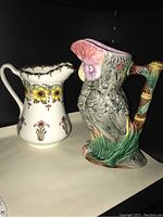 Two ceramic pitchers side by side: one white floral Furnivals Beatrice transferware jug and one parrot-shaped colorful ceramic jug.