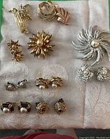 Top-down image showing assortment of costume brooches and earrings laid out on a white textured cloth.
