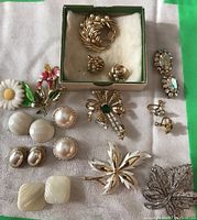 Photo showing 6 brooches and various clip-on earrings arranged on fabric.